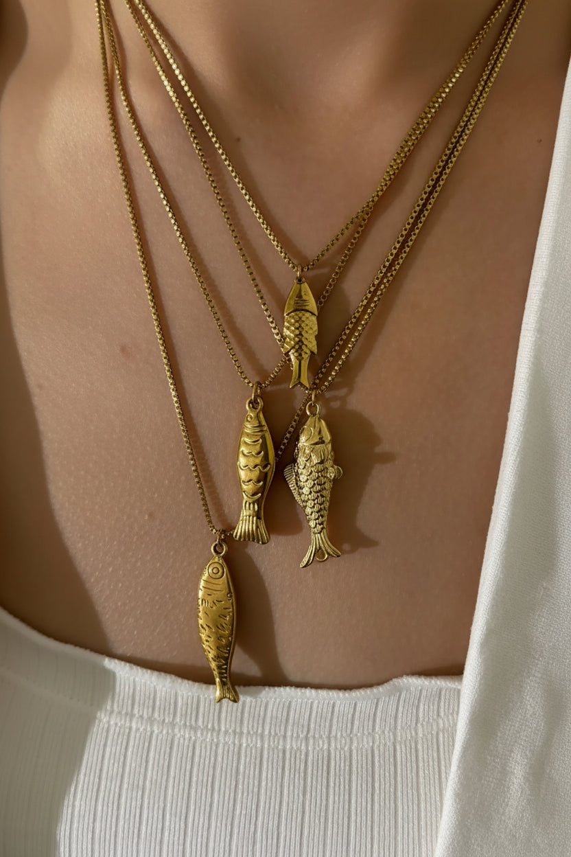 Gold fish-shaped necklaces on a person wearing a white top.