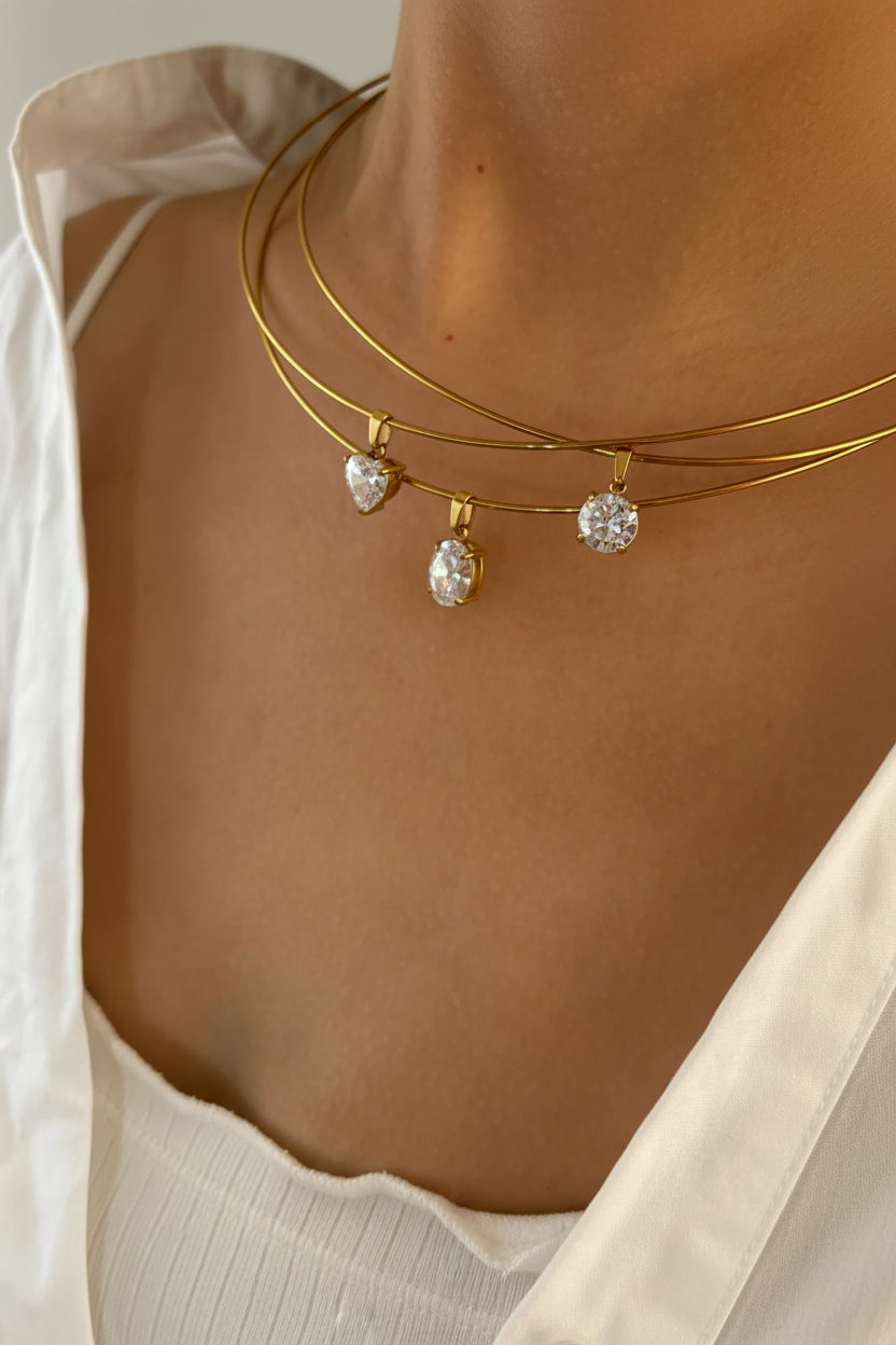 Gold necklaces with heart and round pendants on a person wearing a white top.
